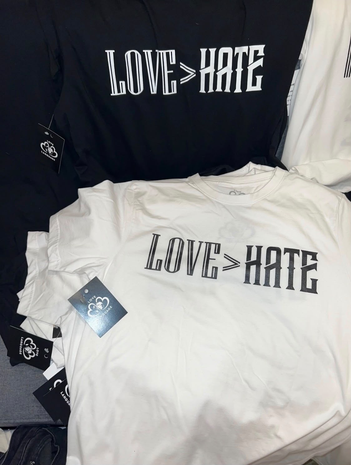 Black and white Love Greater Than Hate tees with Love Language hang tags attached