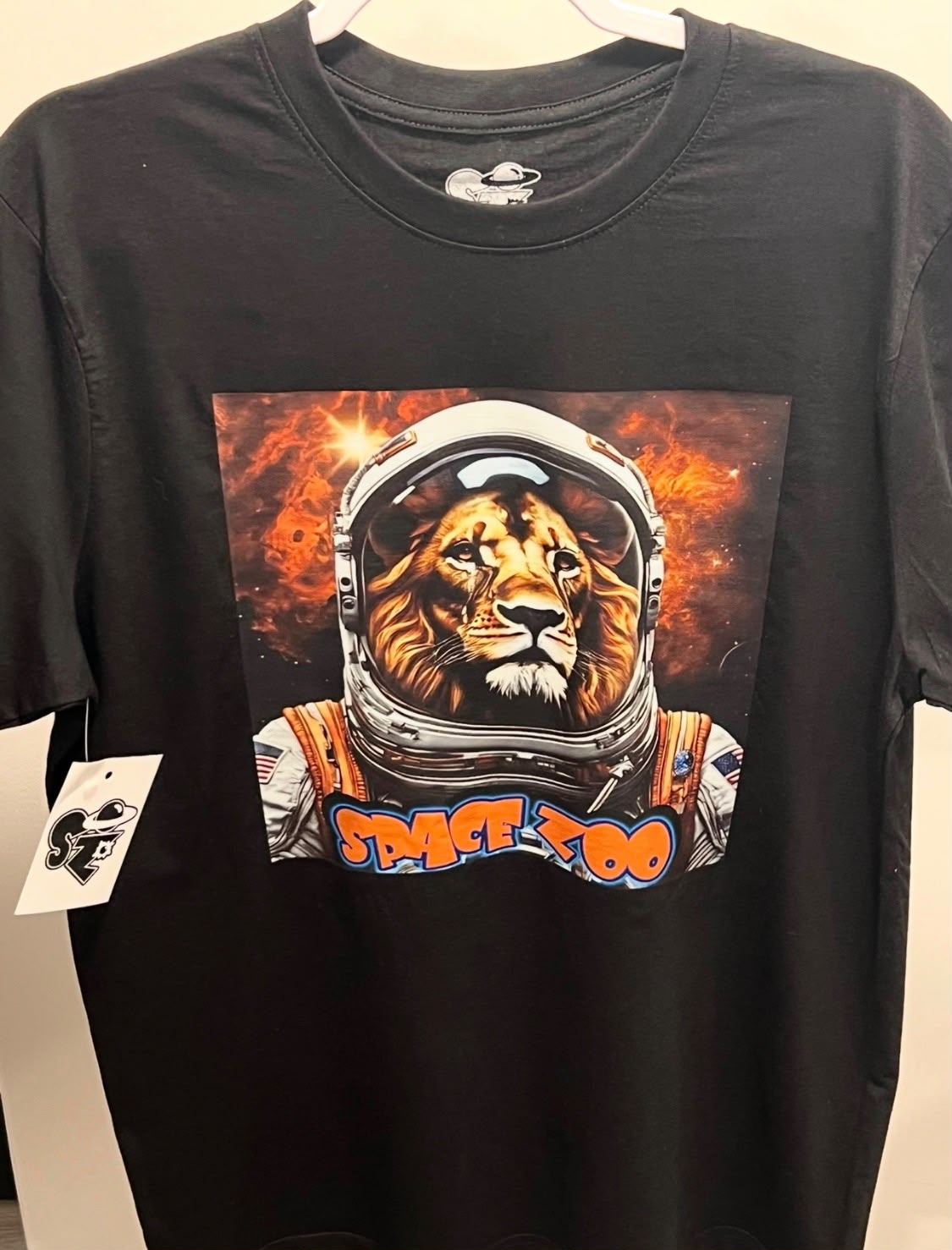 Black Space Zoo t-shirt on a hanger with astronaut lion print and SZ hang tag